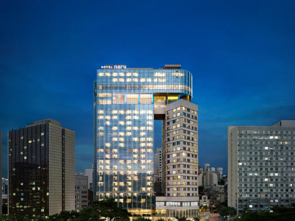 세련된 조명과 현대적인 건축미가 돋보이는 호텔 나루 서울 엠갤러리의 야간 건물 외관입니다.